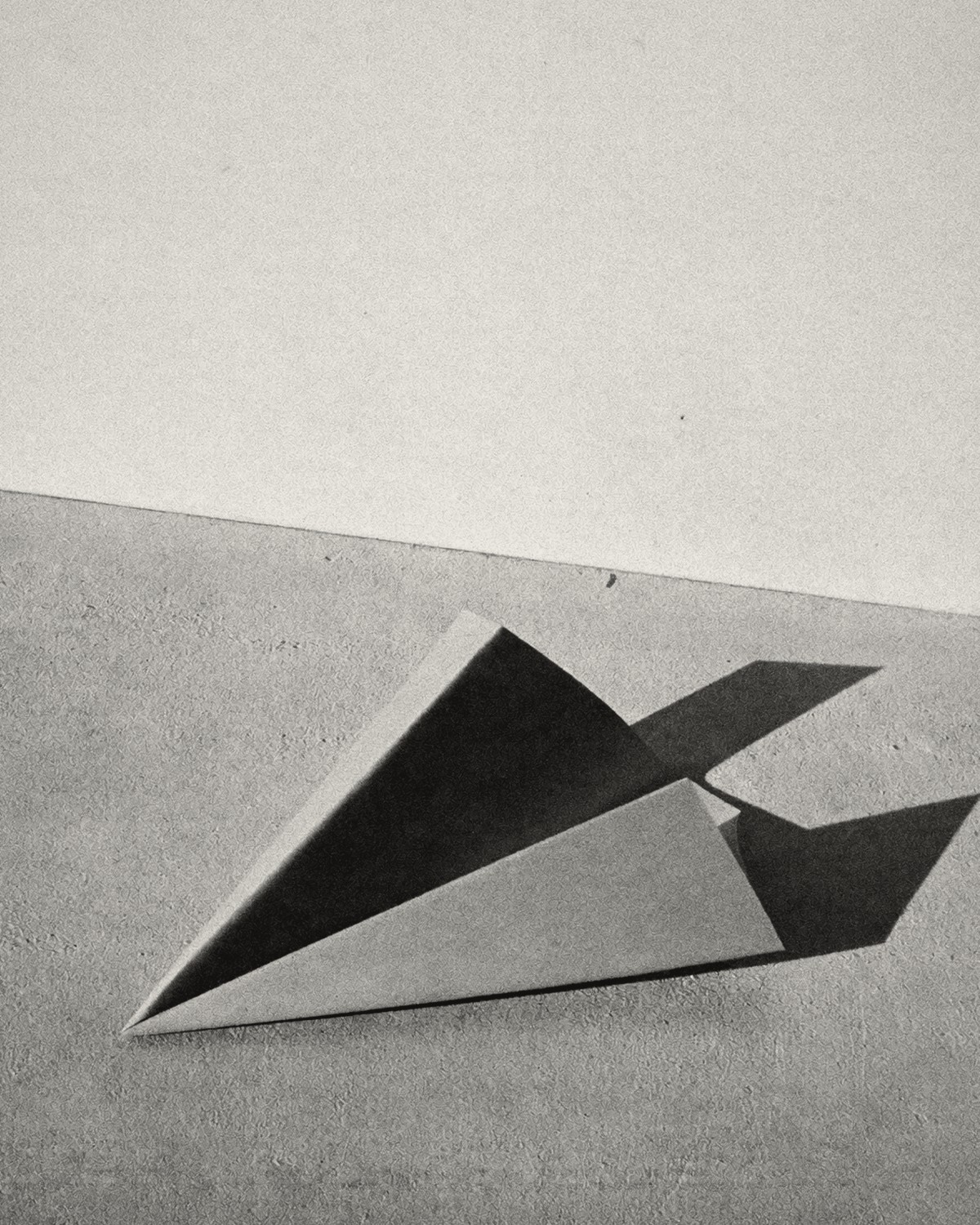 A paper aeroplane resting on a bare floor, throwing a sharp shadow.