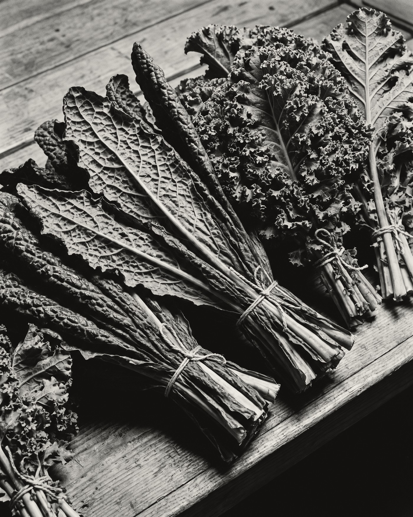 Bunches of kale and chard tied with string on a wooden board.