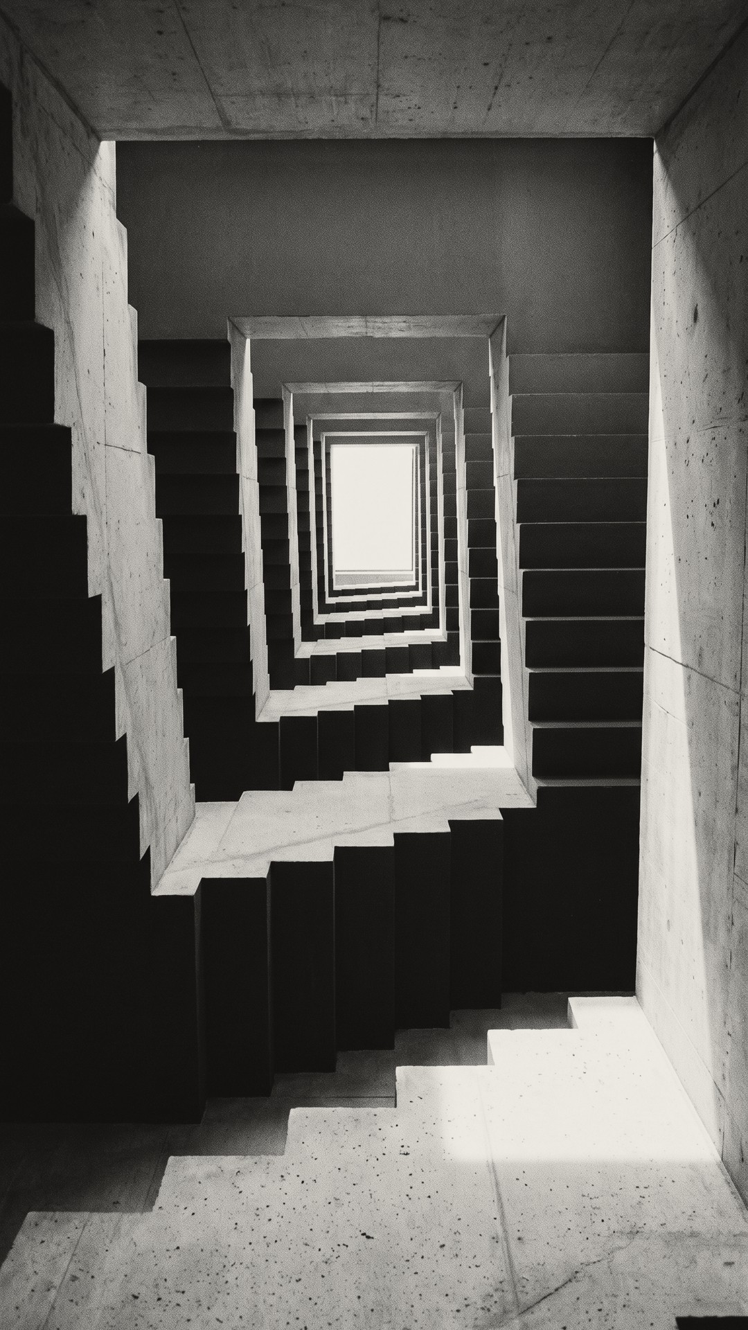 A concrete stairwell squaring upward towards a bright opening at the top.