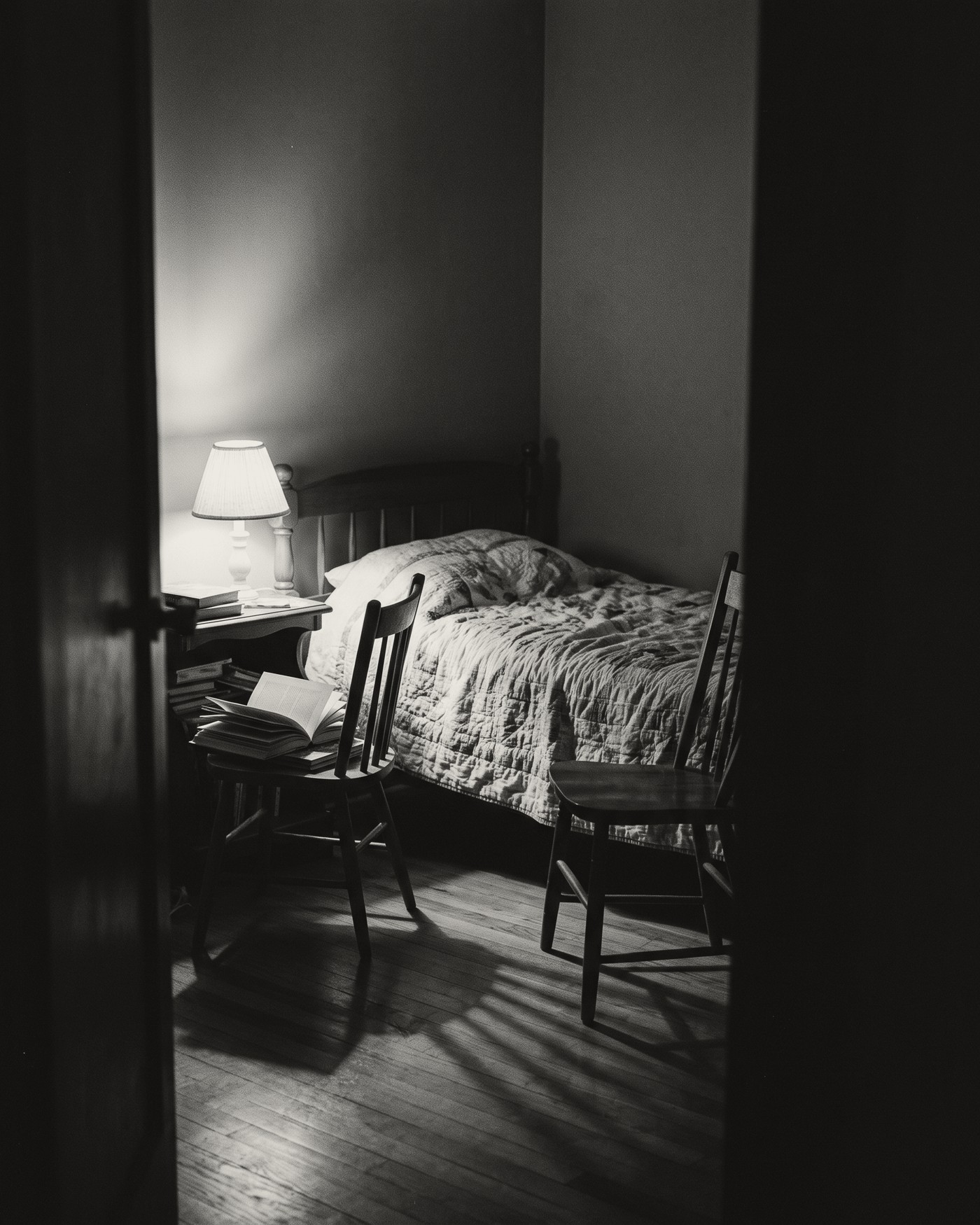 A child&rsquo;s bedroom at night seen from the doorway, a reading lamp lit beside a stack of storybooks and an empty chair pulled up to the bed.